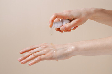 A woman pours serum or oil on her hand to show texture and moisturize the skin on a beige isolated background. The concept of face and skin care. Picture for your design