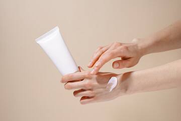 Female hands holding white mockup jar and applying swatch of cream sample on hand on beige isolated...