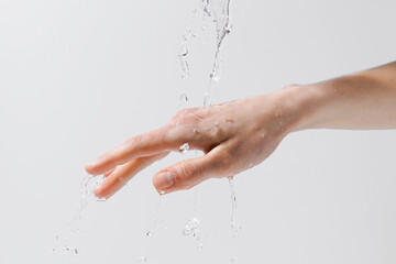 Fototapeta premium Water pouring on a woman's hand on a gray isolated background. The concept of skin hydration and moisture enrichment, anti-aging care. Image for your design