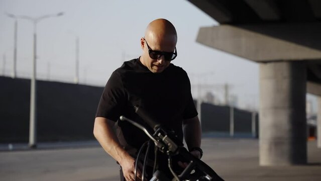 The biker approaches the motorcycle and checks its condition. A brutal man is preparing to get behind the wheel of a black motorcycle.