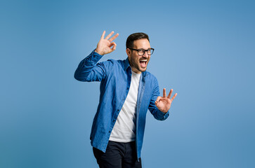 Satisfied businessman gesturing OK sign and shouting while standing against blue background