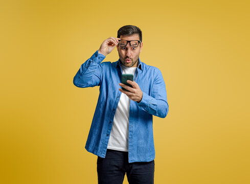 Shocked businessman reading unexpected message over smart phone against yellow background