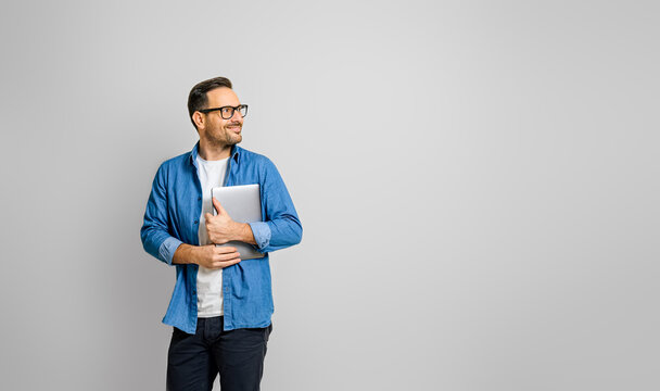 Smiling male professional holding digital tablet looking away thoughtfully against white background