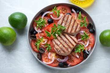 Plate with grilled tuna steaks and mediterranean salad on a light-grey granite background,...