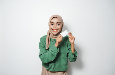 Smiling young Asian Muslim woman dressed in green shirt holding credit card, online shopping isolated over white background
