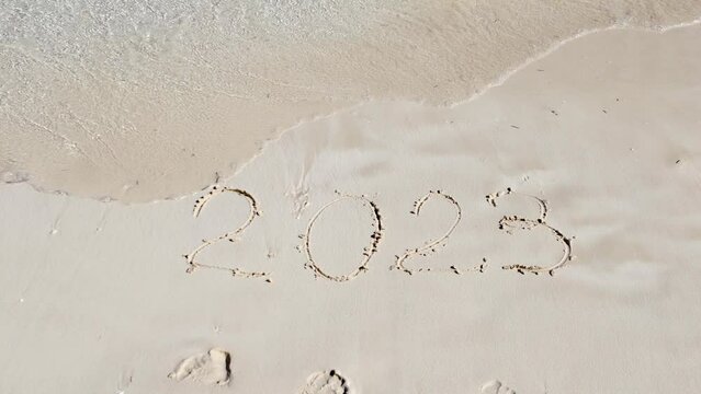 A sea wave washes away the sand next to the inscription 2023.The end of the old and the beginning of the new year.The concept of the outgoing year.Vacation in 2023.The numbers are written in the sand