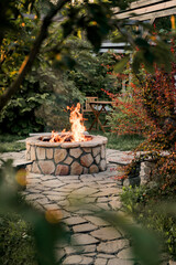 Patio and fire in the fire pit in the evening. Beautiful fire flames surrounded by beautiful trees. In the background is a table and two chairs.