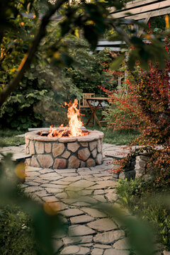 Patio and fire in the fire pit in the evening. Beautiful fire flames surrounded by beautiful trees. In the background is a table and two chairs.
