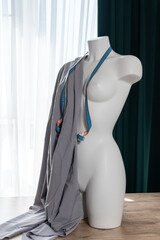 White modern mannequin or dressmakers dummy with gray fabric and hanging measuring tape