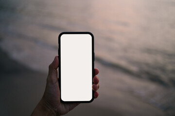 Man hand holding mobile phone with sunset background. White empty space mobile display. Smartphone blank screen mock up image.