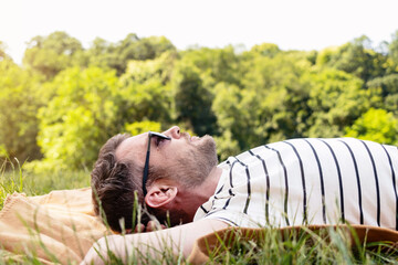 A man in sunglasses is resting in the park, lying on his back on the green grass and looking at the...