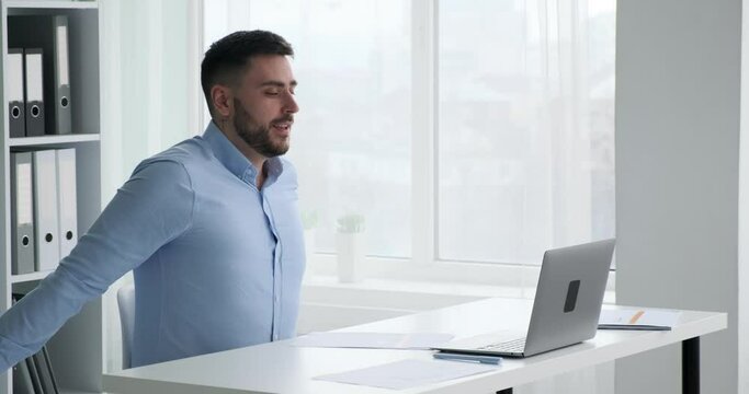 A successful European businessman in business attire is sitting typing on his laptop. He completes his work and lean back on chair, stretching arms and crossing them on his chest.