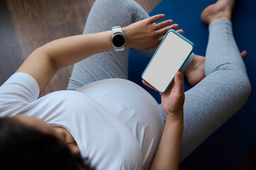 Top view pregnant woman checks smart watch to control pulse and heart rate, relaxing with...