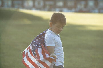 Kid boy celebrating of July, 4 Independence Day of USA . Child running with american flag symbol of United States over wheat field.