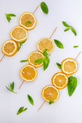 Citrus slices and mint leaves on a wooden skewer. Top view with lemon theme on white background.