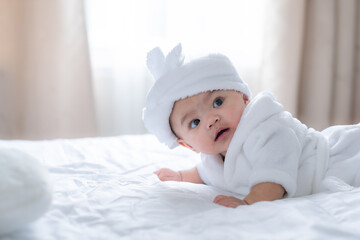 Baby child lie on stomach with head up, cute infant on white bed with blur white curtain and light of morning.