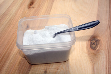 Salt in a plastic container with a spoon inside on the table