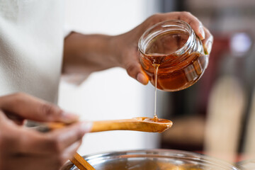 Female hands holding a bowl of bee honey and a wooden spoon. Close up. Elaboration of organic soap...