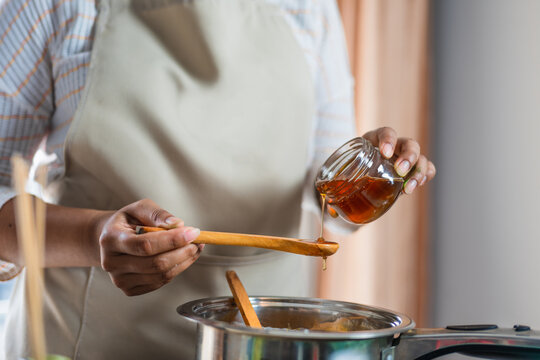 Female hands holding a bowl of bee honey and a wooden spoon. Close up. Elaboration of organic soap based on glycerin.