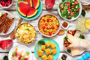 Summer food table scene over a white wood background. Various refreshing salads, fruit, wraps and BBQ grilled skewers. Overhead view.