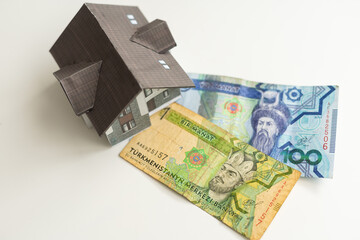 A small house lies on a fan of hundred dollar bills. The keys to the purchased house. Reduced copy of the house on a white background