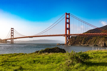 The Golden Gate Bridge over San Francisco Bay as seen from a green meadow overlook. The most famous...