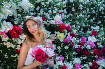 Beautiful happy and sexy young woman, a bride in a white dress enjoys the smell of flowers In a blooming summer garden.