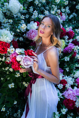Beautiful happy and sexy young woman, a bride in a white dress enjoys the smell of flowers In a blooming summer garden.