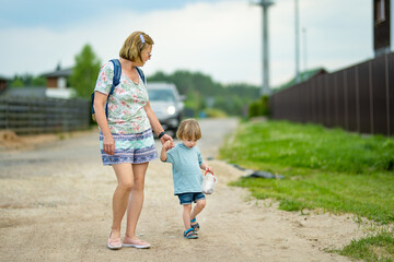 Fototapeta premium Grandmother with her toddler grandson having fun outdoors on beautiful spring day. Grandma taking a walk with her grandchild.