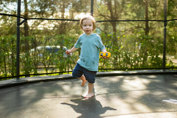 Cute toddler boy jumping on a trampoline in a backyard on warm and sunny summer day. Sports and exercises for children.