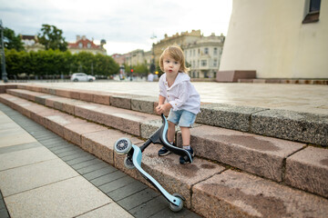 Funny toddler boy riding a baby scooter outdoors on summer day. Kid training balance on mini bike....