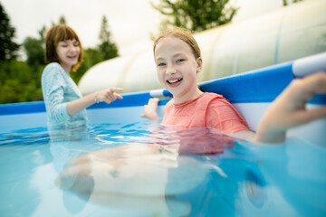 Two funny teenage sisters trying to get into cold pool water. Children having fun in outdoor pool. Summer activities for the family with kids.