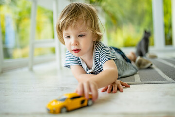 Cute toddler boy playing with yellow toy car. Small child having fun with toys. Kid spending time in a cozy living room at home.