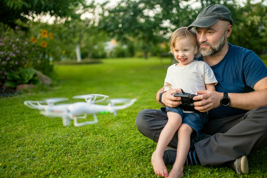 Father and son watching and navigating a drone. Cute toddler boy helping his father to operate a drone by remote control. - Powered by Adobe