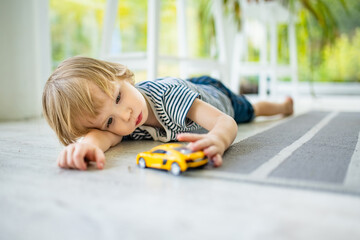 Cute toddler boy playing with yellow toy car. Small child having fun with toys. Kid spending time in a cozy living room at home.