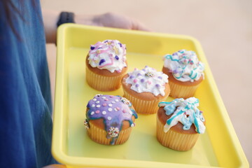kids home made cupcakes. many cupcakes with decoration, sprinkles and white frosting on a yellow tray.