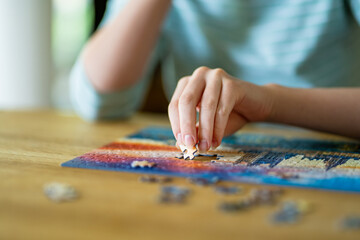 Close-up on woman hand playing puzzles at home. Connecting jigsaw puzzle pieces in a living room...