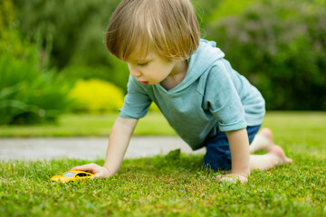 Cute toddler boy playing with yellow toy car outdoors. Kid exploring nature. Small child having fun with toys.