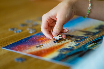 Close-up on woman hand playing puzzles at home. Connecting jigsaw puzzle pieces in a living room...