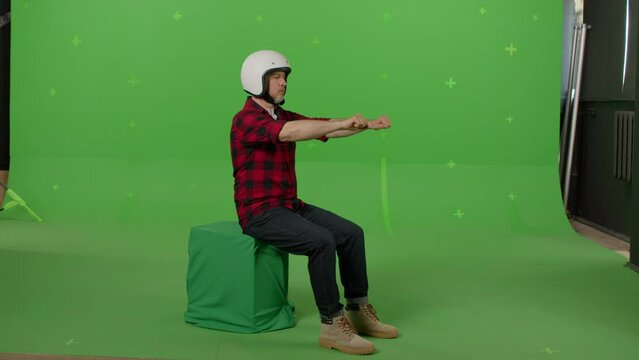 Man wearing a motorcycle helmet and pretending to drive a motorbike on a green background in the studio