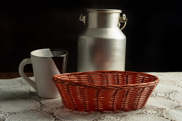 Obraz na płótnie Canvas Empty basket, mug and bucket of milk on white lace tablecloth, dark background, selective focus.