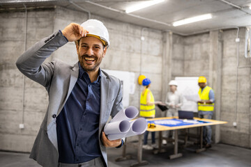 Portrait of smiling caucasian civil engineer holding project plans at construction site. - obrazy, fototapety, plakaty