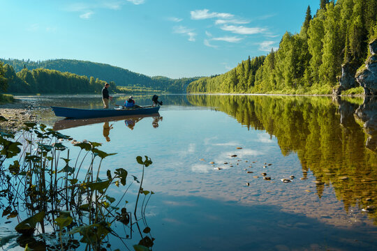 Two fishermen, father and son, are preparing for morning fishing near a motor boat in the summer on a mountain river in good sunny weather. Rest on the river in the men's company. River rafting