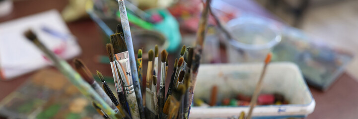 Paint brushes in glasses at artist workplace