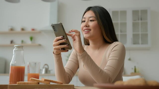 Asian chinese japanese woman girl housewife in home kitchen use mobile phone apps choose food delivery make order online buy grocery typing message cellphone texting search cooking recipe glad smiling