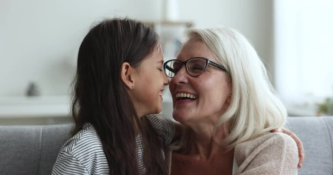 Loving mature grandmother feeling unconditional love to little granddaughter touch noses, laughing, enjoy sweet life moments of tenderness, close up faces. Multi-generational family bonding and ties