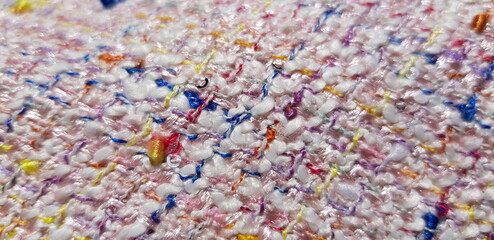 Wavy light pink tweed fabric (boucle) with a small patterned weave, in the sun (macro, top view, texture).