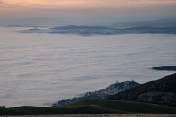 Aerial view of Assisi Umbria Italy above a sea of fog at dusk - 611780142