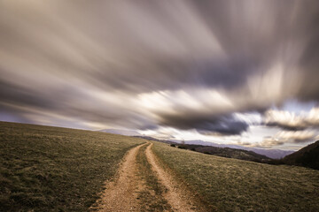 Spectacular long exposure view of clouds above a path on a hill - 611780794