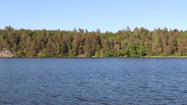 A nice view over dark calm water. Part of the Swedish lake Malar or Malaren. Which is next to the Baltic sea. Summer time with a forest in the background. Clear blue sky. Jarfalla, Stockholm, Sweden